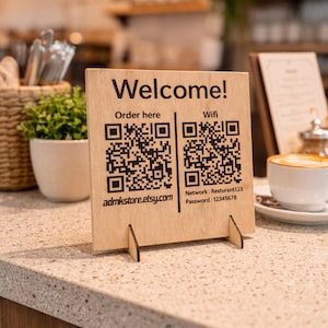 Peut inclure: Panneau en bois avec le mot "Bienvenue !" en noir. Le panneau comporte deux codes QR, un pour commander et un pour l'accès au Wi-Fi. Le réseau et le mot de passe Wi-Fi sont indiqués sous le code QR. Le nom de la boutique Etsy est également imprimé.