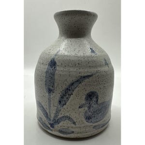 Può includere: Un vaso in ceramica con smalto bianco sporco maculato caratterizzato da un disegno blu dipinto a mano di un'anatra che nuota vicino a giunchi. Il vaso ha un corpo arrotondato e un collo stretto e svasato con una finitura testurizzata.