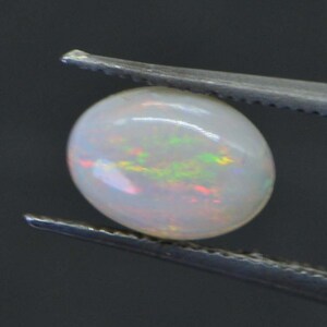May include: A white opal gemstone with iridescent flashes of color, held by tweezers.