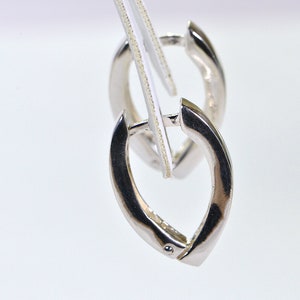 Puede incluir: Un par de pendientes de aro de plata con forma redonda y lisa. Los pendientes se muestran sobre un fondo blanco.