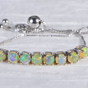 May include: A silver chain bracelet with a sliding clasp and a row of round, iridescent opal gemstones.