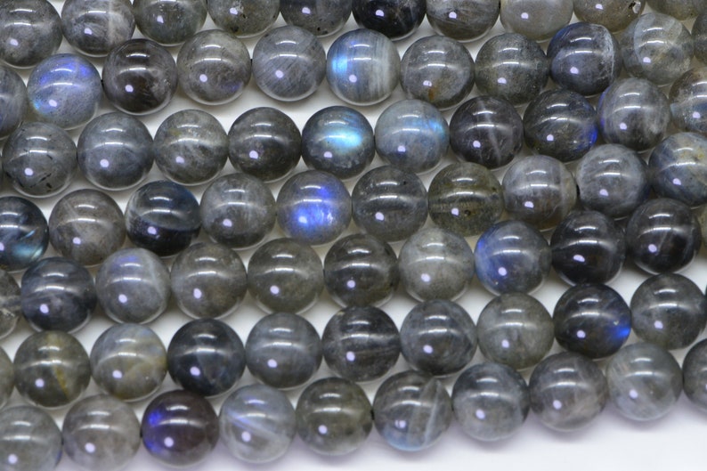 May include: A strand of round, grey labradorite beads with iridescent blue flashes. The beads are smooth and polished.