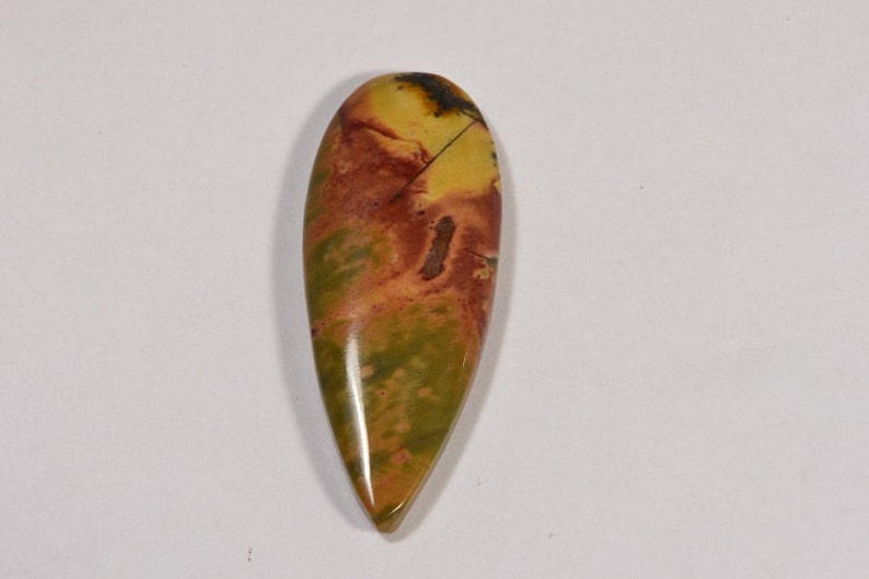 May include: A polished, teardrop-shaped gemstone with a blend of colors. The stone features a base of olive green, transitioning to shades of orange and yellow, with dark brown veining. The gemstone is smooth and glossy.