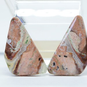 May include: Two triangular shaped agate cabochons with a mix of brown, white, and green colors. The cabochons have a polished surface and are ready to be set in jewelry.