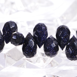 May include: A strand of dark blue gemstone beads with a faceted, teardrop shape. The beads have a sparkly, speckled appearance.