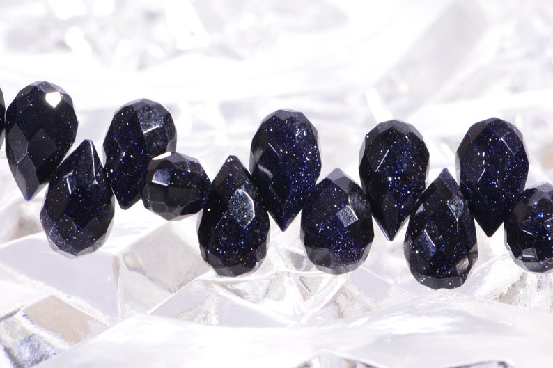May include: A strand of dark blue gemstone beads with a faceted, teardrop shape. The beads have a sparkly, speckled appearance.