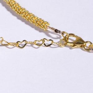 May include: Gold chain necklace with a white bead and heart-shaped links. The necklace has a lobster clasp closure.