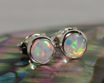 May include: A pair of silver stud earrings with round opal gemstones. The opals have a white base with iridescent flashes of green, blue, and pink.