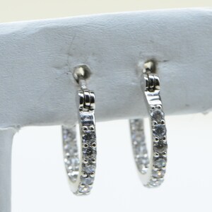 May include: A pair of silver hoop earrings with small clear stones set around the entire hoop.