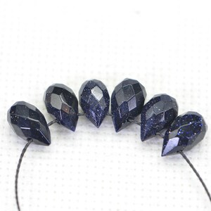 May include: A strand of dark blue gemstone beads with a faceted teardrop shape. The beads are strung on a black thread.