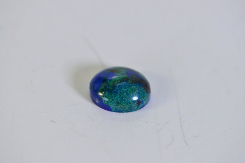 May include: A round, blue and green gemstone cabochon with a smooth, polished surface.