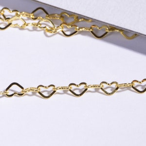 May include: A gold heart-shaped chain with a delicate design. The chain is made of small, interconnected heart-shaped links.