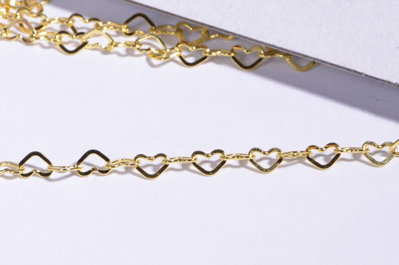 May include: A gold heart-shaped chain with a delicate design. The chain is made of small, interconnected heart-shaped links.