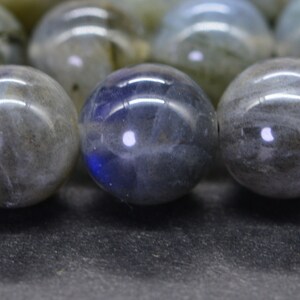 May include: A close-up of a strand of round, grey and blue labradorite beads. The beads are smooth and polished, with a slight iridescent sheen.
