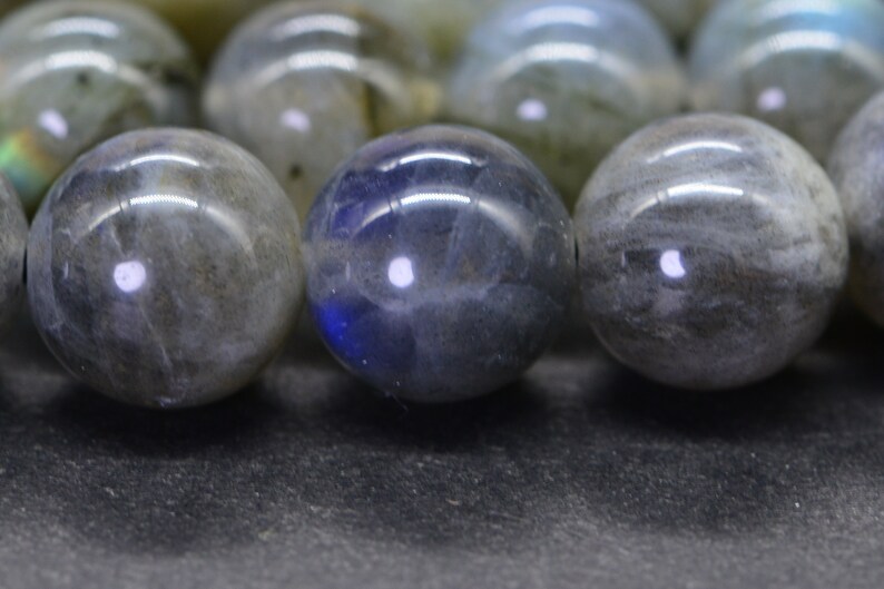 May include: A close-up of a strand of round, grey and blue labradorite beads. The beads are smooth and polished, with a slight iridescent sheen.