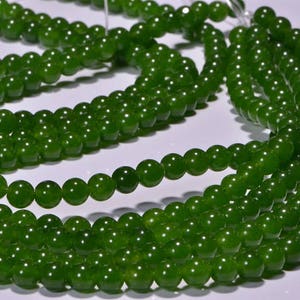 May include: A strand of green jade beads, with a smooth, polished finish. The beads are round and uniform in size, and they are strung together on a clear thread.