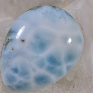 May include: A light blue cabochon gemstone with a swirling, marbled pattern. The stone has a smooth, polished surface and is set against a white background.
