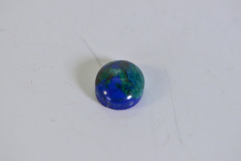May include: Oval-shaped gemstone with a blue and green color pattern. The gemstone has a smooth, polished surface.