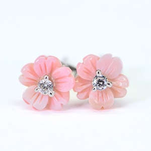 Puede incluir: Un par de pendientes de color rosa en forma de flor con un pequeño diamante en el centro de cada flor.