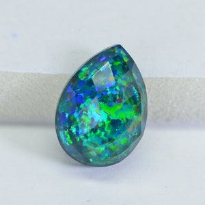 May include: A teardrop-shaped, faceted opal gemstone with a dark blue, green, and iridescent finish.