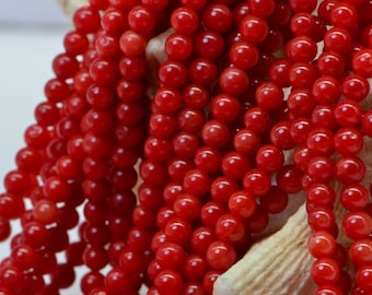 May include: A strand of bright red coral beads. The beads are round and smooth, and they are strung together on a clear thread.