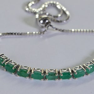 Puede incluir: Un brazalete de cadena de plata con una engaste de piedras preciosas de esmeralda verde. El brazalete tiene un cierre ajustable.