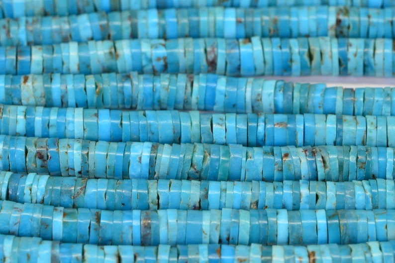 May include: A strand of turquoise beads, each bead is a flat, rectangular shape with rounded edges. The beads are a vibrant blue color with brown and white marbling.