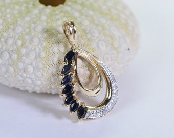 May include: A gold pendant with a teardrop shape, featuring a row of black gemstones and a smaller circle of clear gemstones.