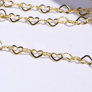 May include: A gold chain necklace with heart-shaped links. The chain is delicate and dainty, perfect for layering with other necklaces.