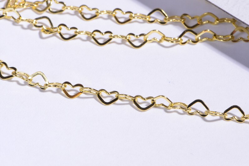 May include: A gold chain necklace with heart-shaped links. The chain is delicate and dainty, perfect for layering with other necklaces.