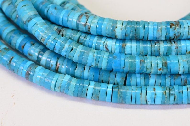 May include: A strand of turquoise beads, each bead is a flat, round disc with a light blue color. The beads are stacked on top of each other, creating a layered effect.