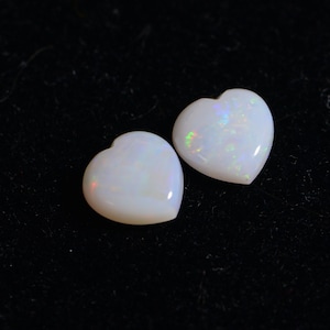 May include: Two white heart-shaped opal gemstones with iridescent rainbow flashes.