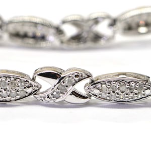Op de afbeelding: Een zilveren armband met een delicaat kettingontwerp. De armband is versierd met kleine, glinsterende diamanten.