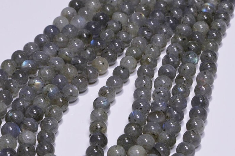 May include: A strand of grey labradorite gemstone beads. The beads are round and have a smooth, polished finish. The labradorite has a subtle iridescent sheen.