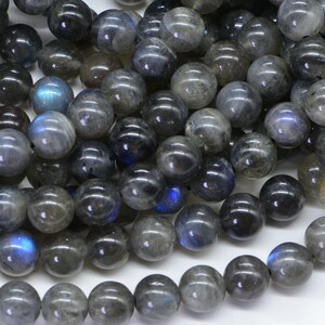 May include: A strand of dark grey labradorite gemstone beads with iridescent blue flashes. The beads are round and smooth, and they are strung on a clear thread.