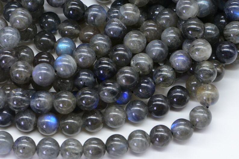 May include: A strand of dark grey labradorite gemstone beads with iridescent blue flashes. The beads are round and smooth, and they are strung on a clear thread.