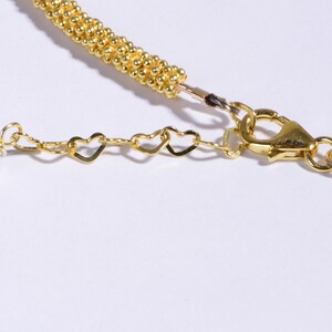 May include: Gold necklace with a heart-shaped chain and a white bead. The necklace has a lobster clasp closure.