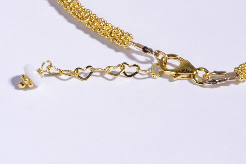 May include: Gold necklace with a heart-shaped chain and a white bead. The necklace has a lobster clasp closure.