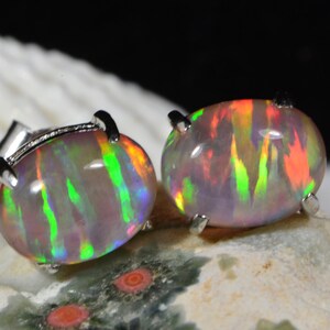 May include: A pair of silver opal earrings with a rainbow iridescent finish. The opals are oval shaped and set in a silver bezel.
