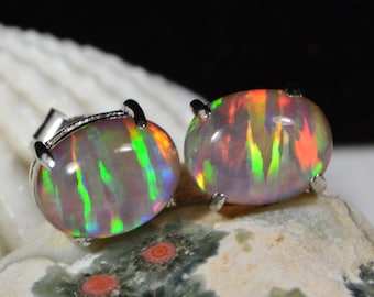 May include: A pair of silver opal earrings with a rainbow iridescent finish. The opals are oval shaped and set in a silver bezel.