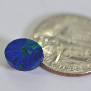 May include: A small, round, blue and green gemstone cabochon, about the size of a US quarter.