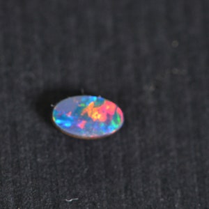 May include: A small oval-shaped opal gemstone with a rainbow of colours, including blue, green, red, and orange.