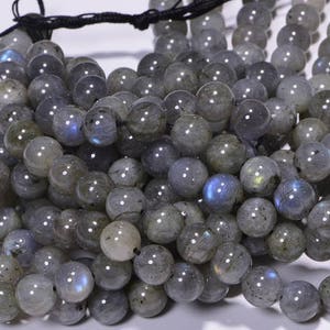 May include: A strand of grey labradorite gemstone beads. The beads are round and have a smooth, polished finish. The labradorite has an iridescent sheen, with flashes of blue, green, and gold.