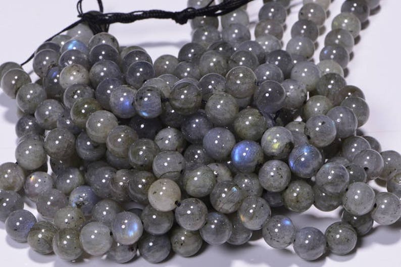 May include: A strand of grey labradorite gemstone beads. The beads are round and have a smooth, polished finish. The labradorite has an iridescent sheen, with flashes of blue, green, and gold.