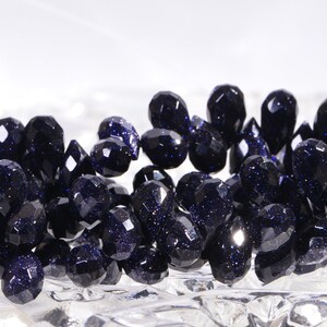 May include: A strand of dark blue faceted gemstone beads. The beads are teardrop shaped and have a sparkly, glittery finish.
