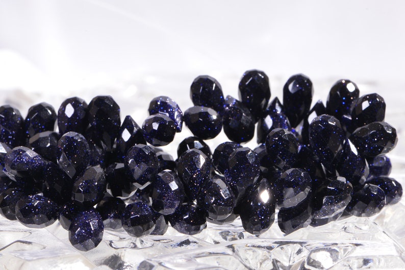 May include: A strand of dark blue faceted gemstone beads. The beads are teardrop shaped and have a sparkly, glittery finish.