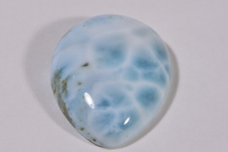 May include: A teardrop-shaped cabochon of blue and white ocean jasper with a smooth, polished surface.