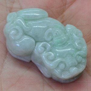 May include: A light green jade pendant carved in the shape of a mythical creature with intricate details.
