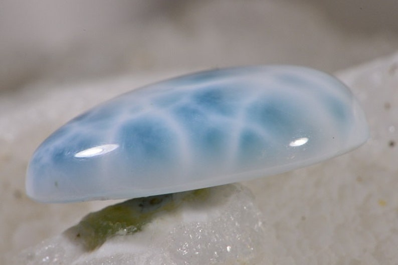 May include: A light blue cabochon gemstone with a swirling, cloudy pattern. The gemstone is smooth and polished.