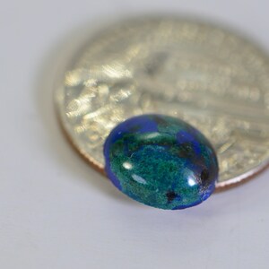 May include: A close-up of a green and blue oval-shaped gemstone, approximately the size of a US quarter.